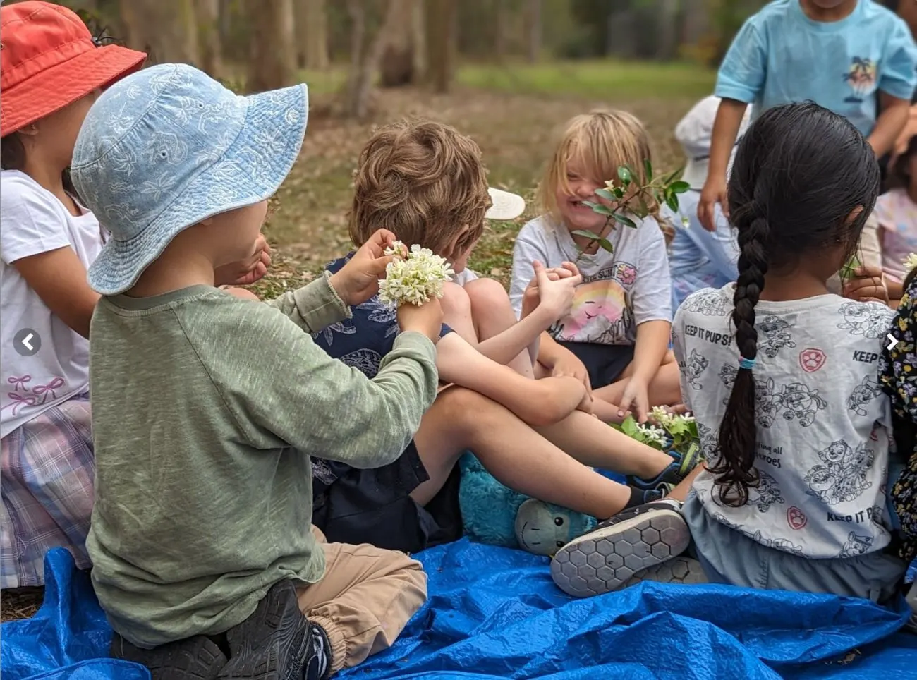 Children sitting together on the picnic tarp sharing native flowers they have found