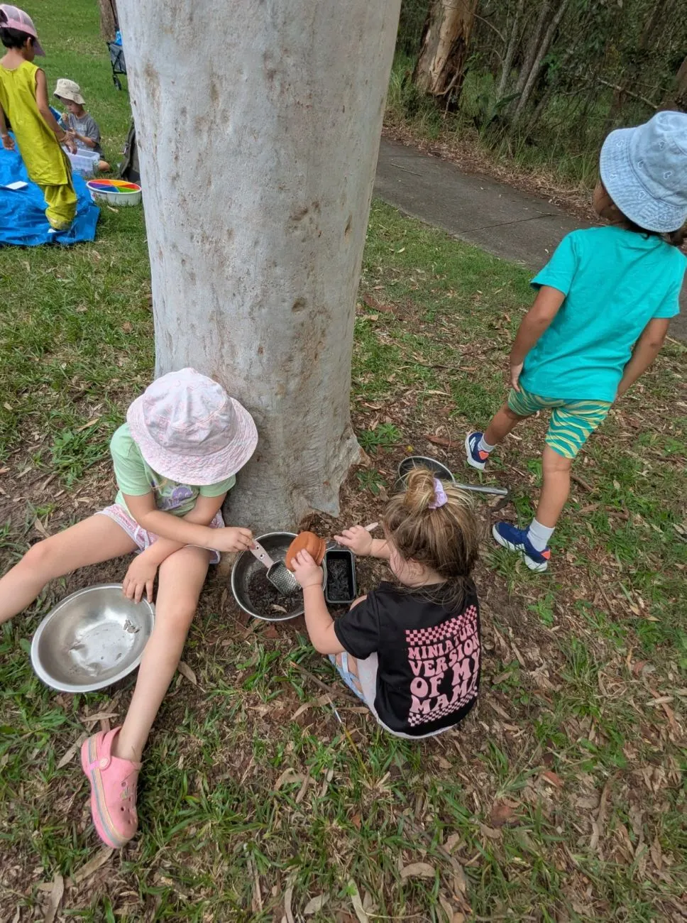 Children painting on clipboards on a blanket in the bush