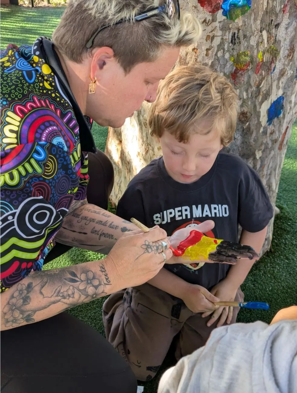 A visiting artist painting a child's hand in red, yellow and black