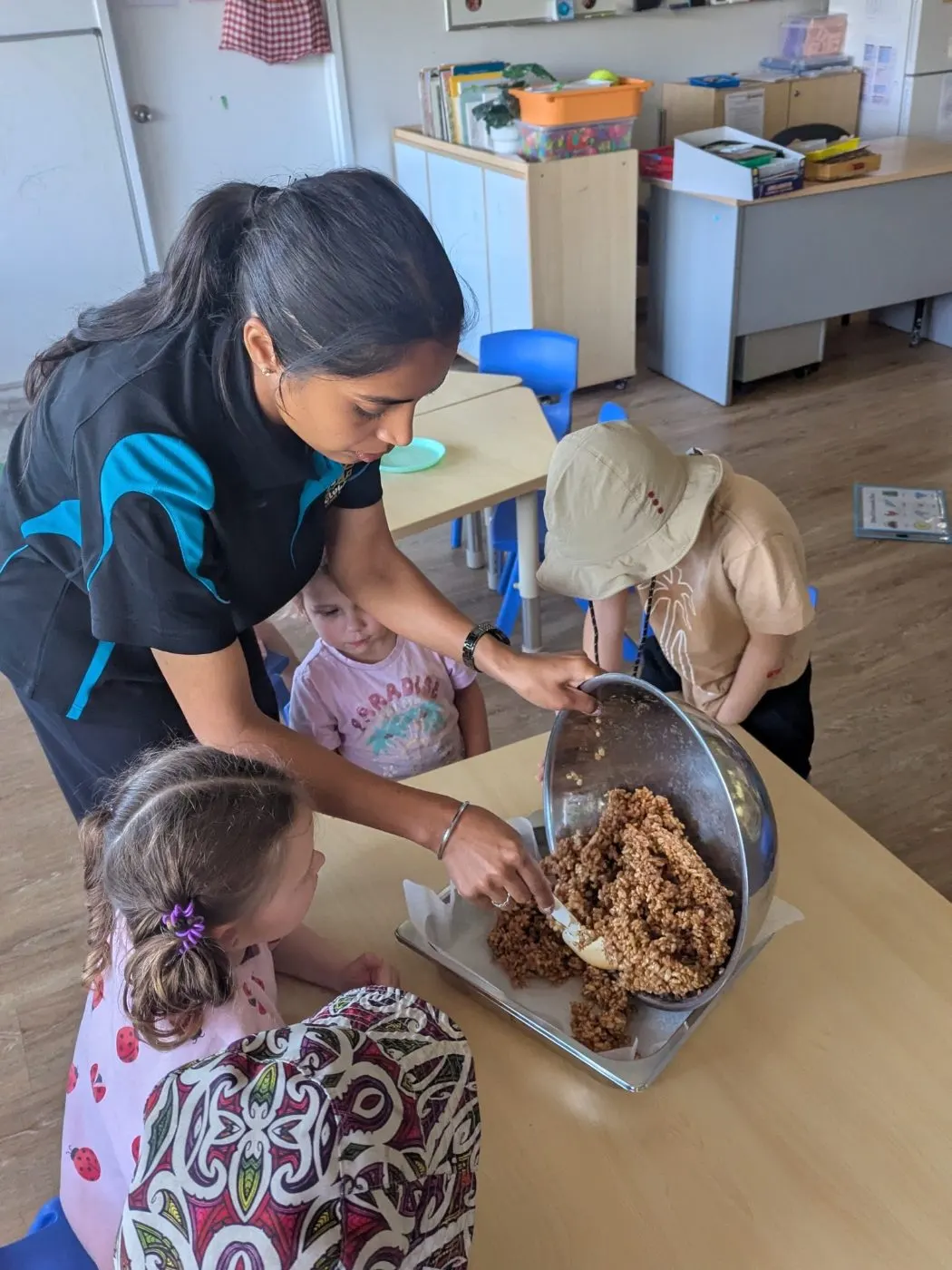 An educator pressing a tray of muesli slice while children watch