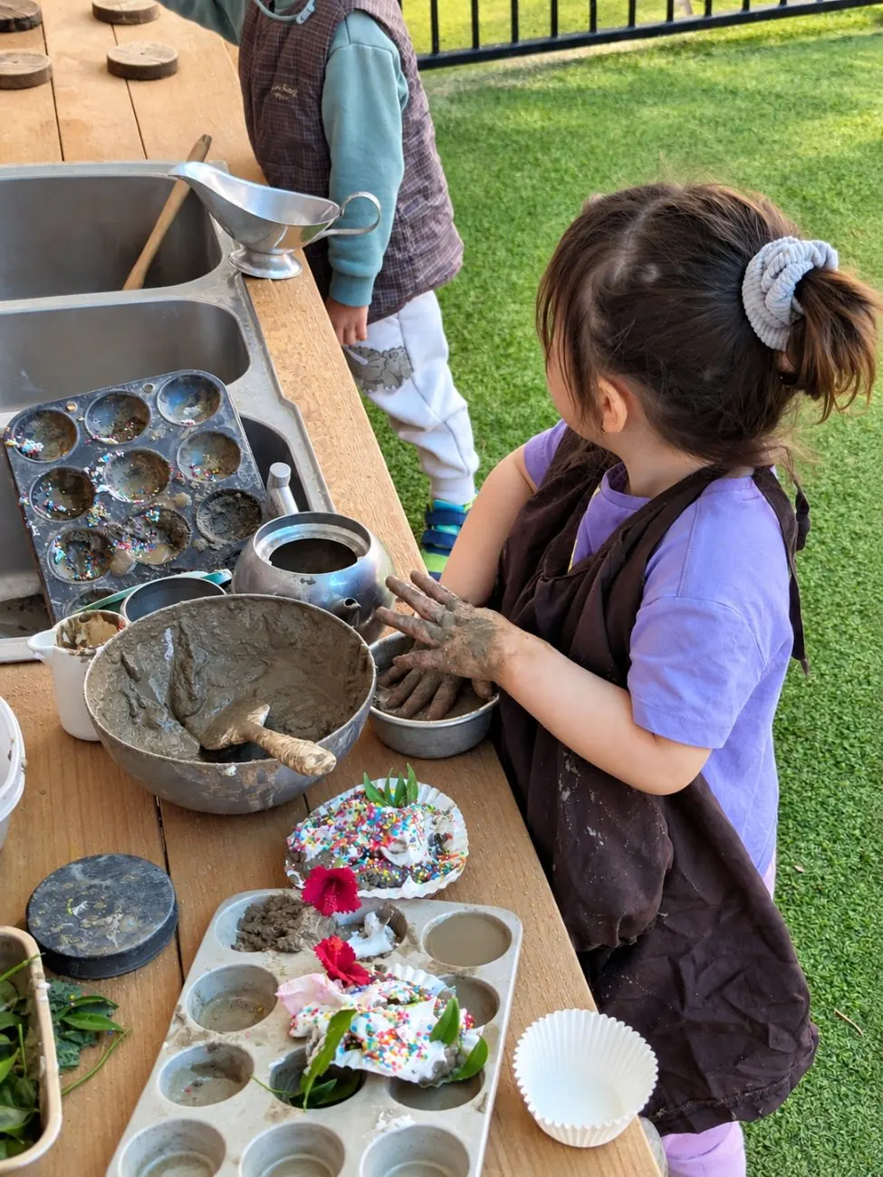 A child pressing mud cakes with sprinkles and flowers at the outdoor mud kitchen
