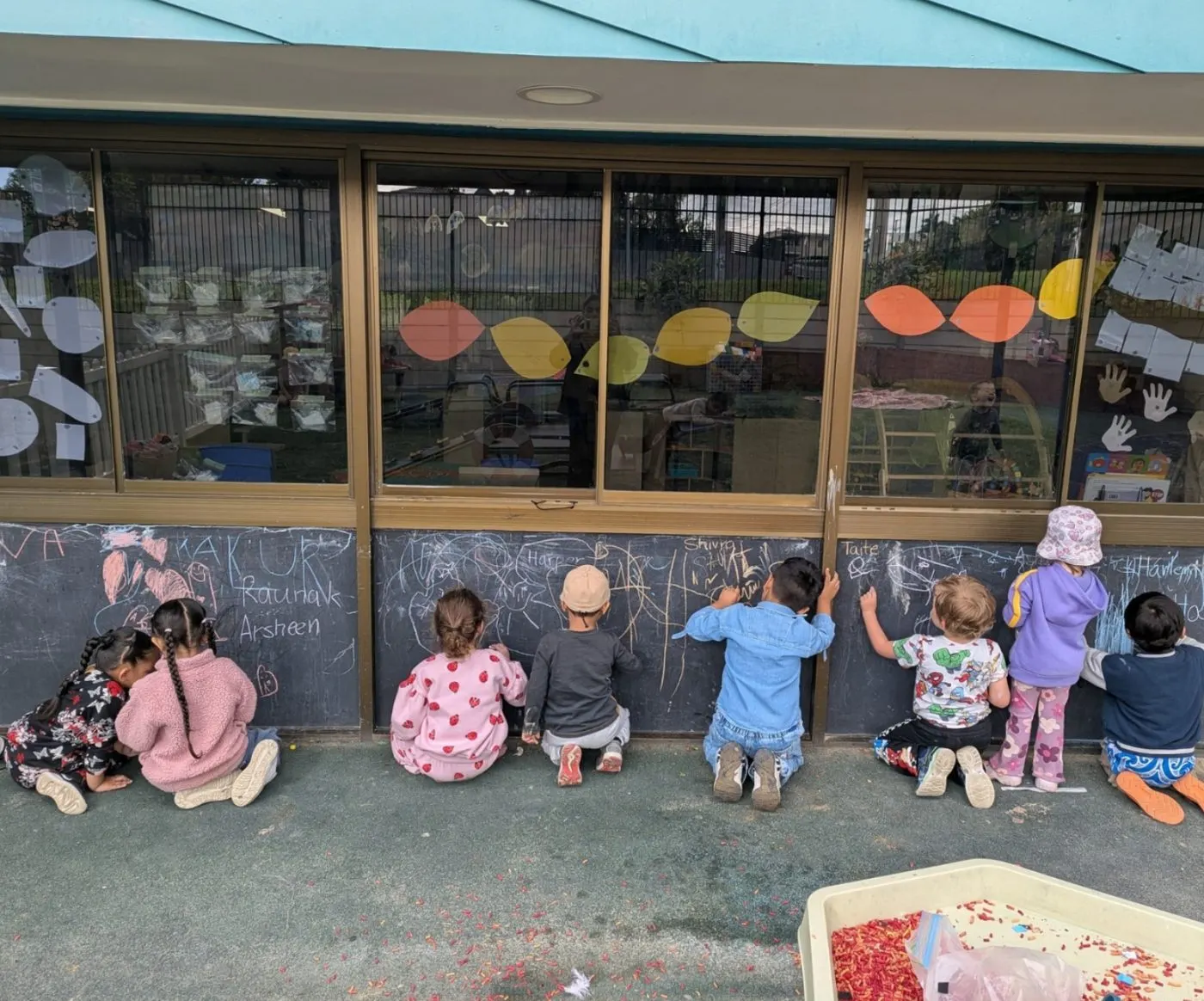 A row of children drawing with chalk on the outdoor chalkboard wall