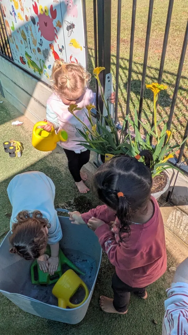 Children watering the garden pots and washing up in a tub outside