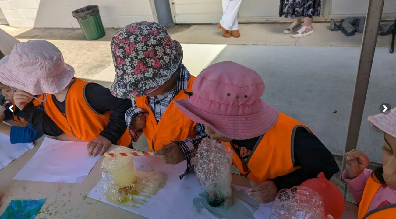 Children blowing coloured bubble paint through straws outside