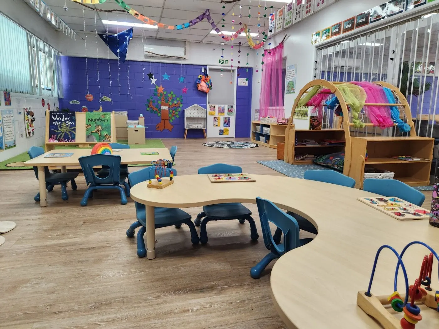 The toddler room, with low tables, a reading corner and the timber cubby