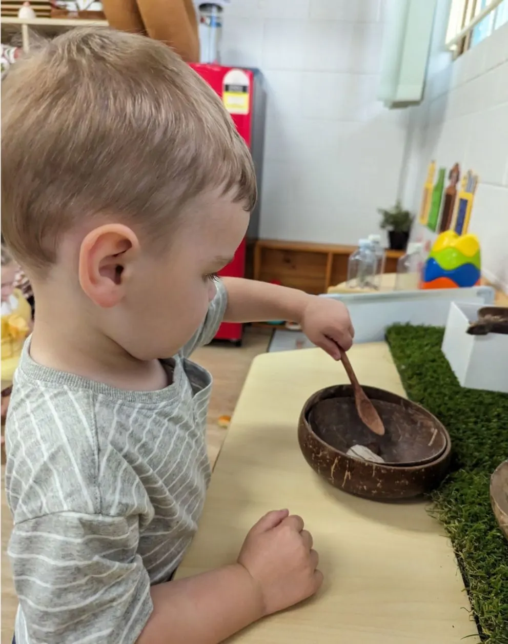 A toddler stirring a coconut bowl at the indoor play kitchen