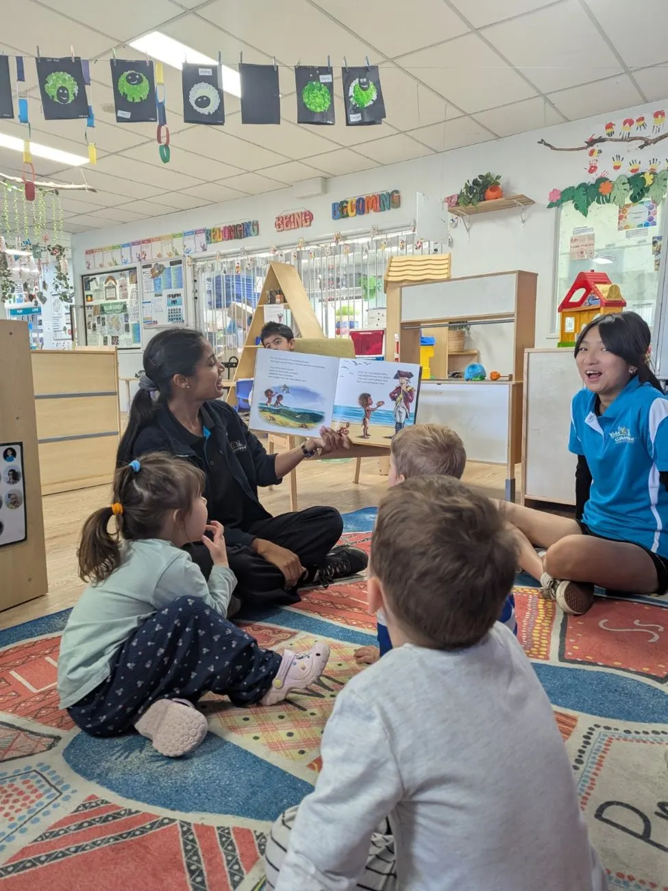 Educators reading a picture book to the toddler group on the mat