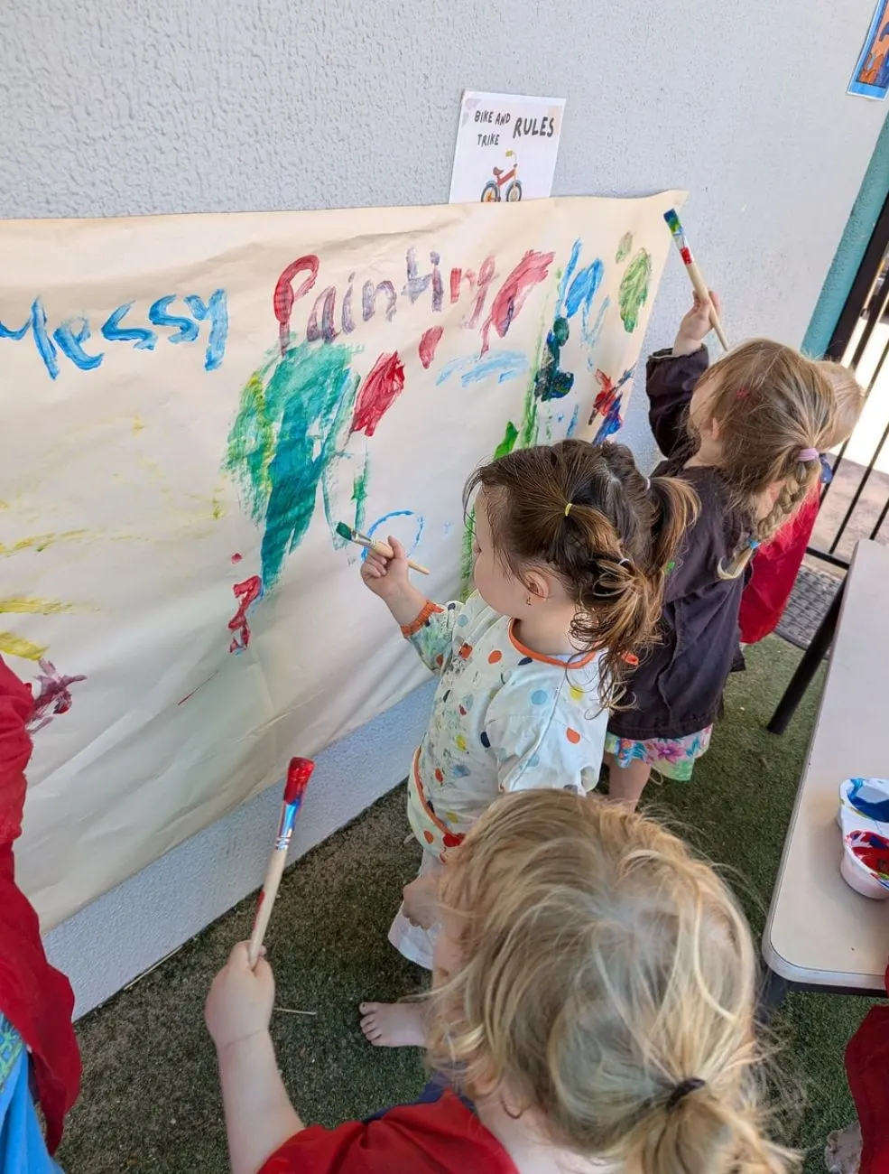 Toddlers painting together on a big sheet of paper labelled messy painting