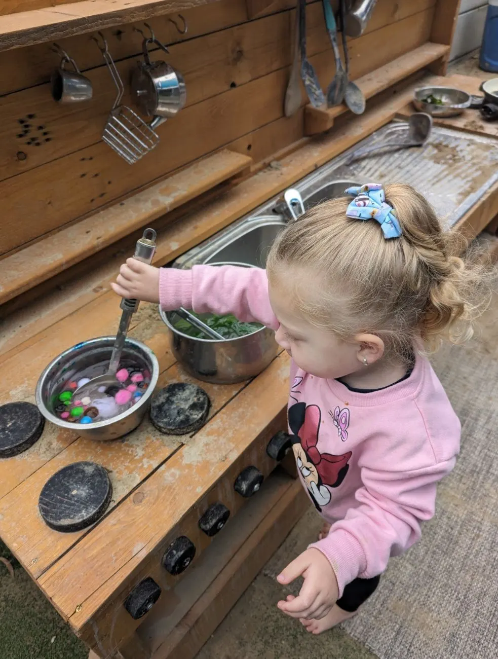 A toddler stirring a bowl at the outdoor mud kitchen