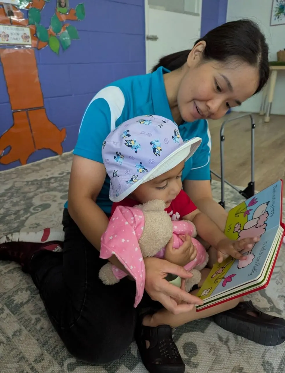 An educator reading a picture book with a toddler on her lap