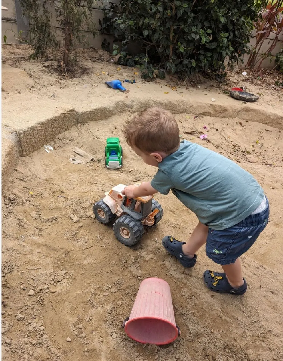 A toddler scooping sand into a pan in the sandpit